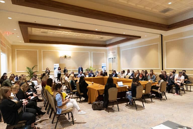 A group of people sitting at an AIM Reimagine conference presentation.