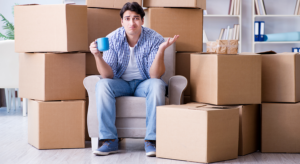 An apartment resident sitting in a chair and shrugging while surrounded by packed boxes