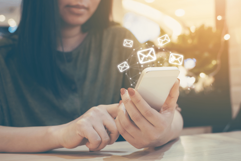 Closeup of a woman holding a phone that has email graphics floating above it