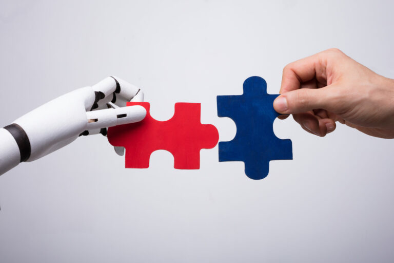 Close-up Of Robot And Human Hand Holding Red And Blue Jigsaw Puzzle