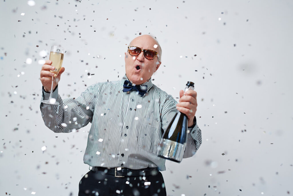 Senior citizen popping a bottle of champagne and throwing confetti