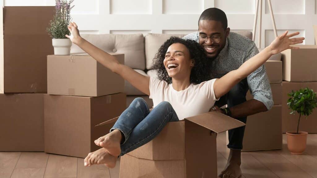 Husband pushing wife in a cardboard box as they move into their apartment