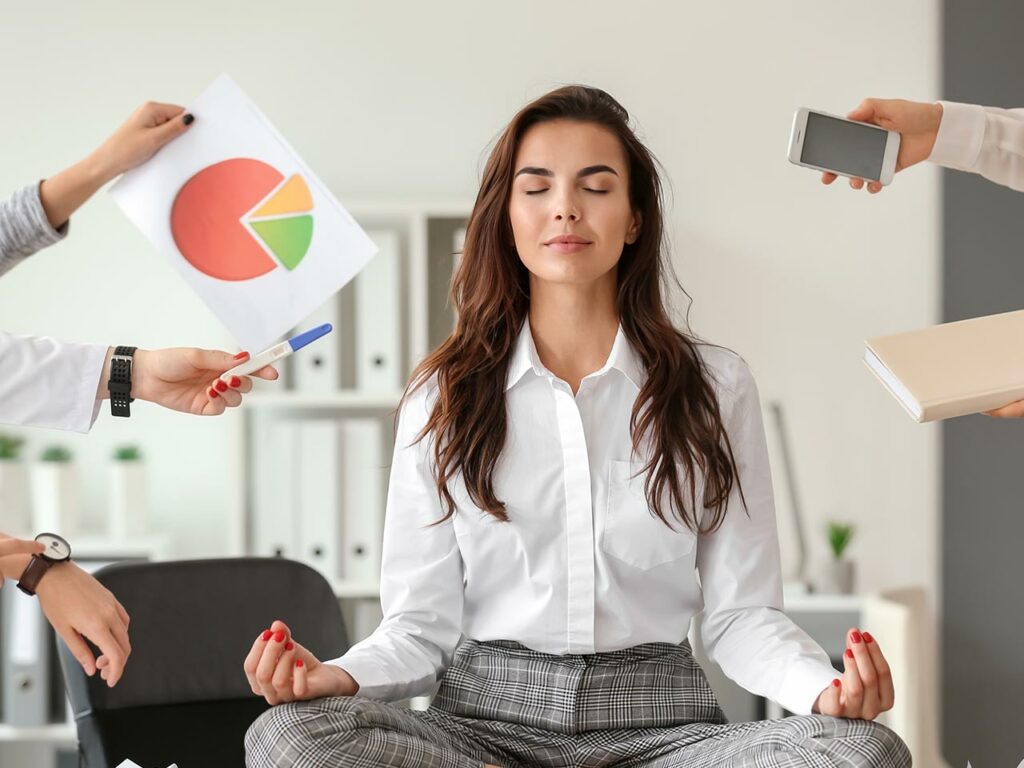 Businesswoman meditating as people hand her multiple devices and reports
