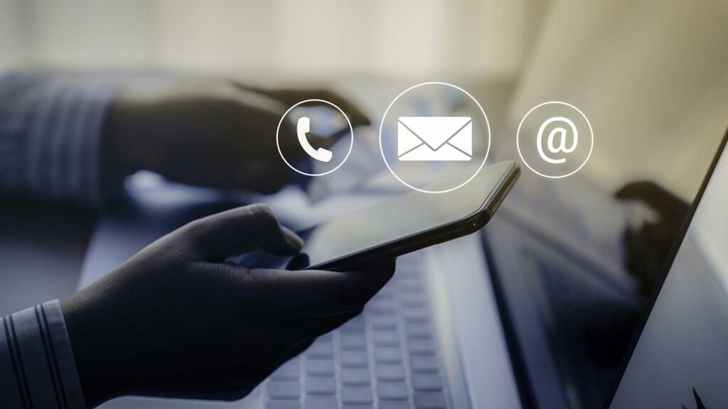 Hand using a cellphone seated before a laptop