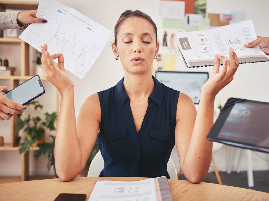 Businesswoman meditating as people hand her multiple devices and reports