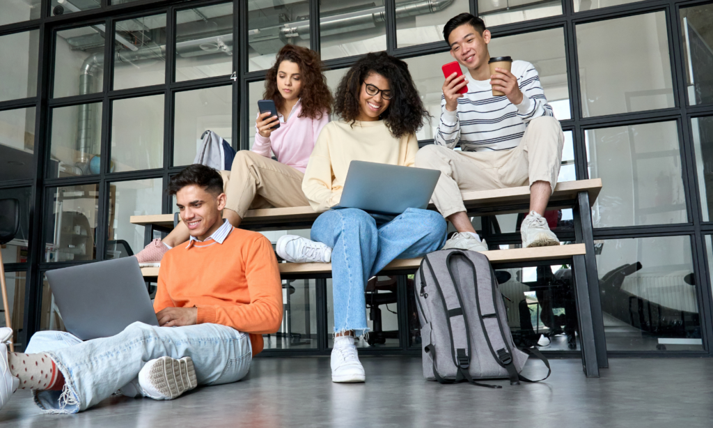 A group of Gen Z young people sitting at a table on electronic devices.